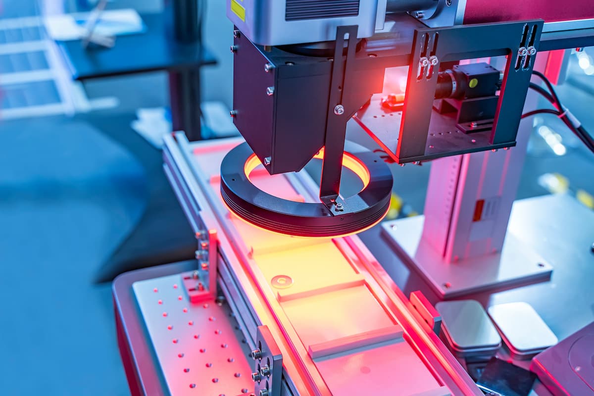 Close-up of an industrial machine performing an automated process, with a red light illuminating a circular object under inspection on a conveyor system.