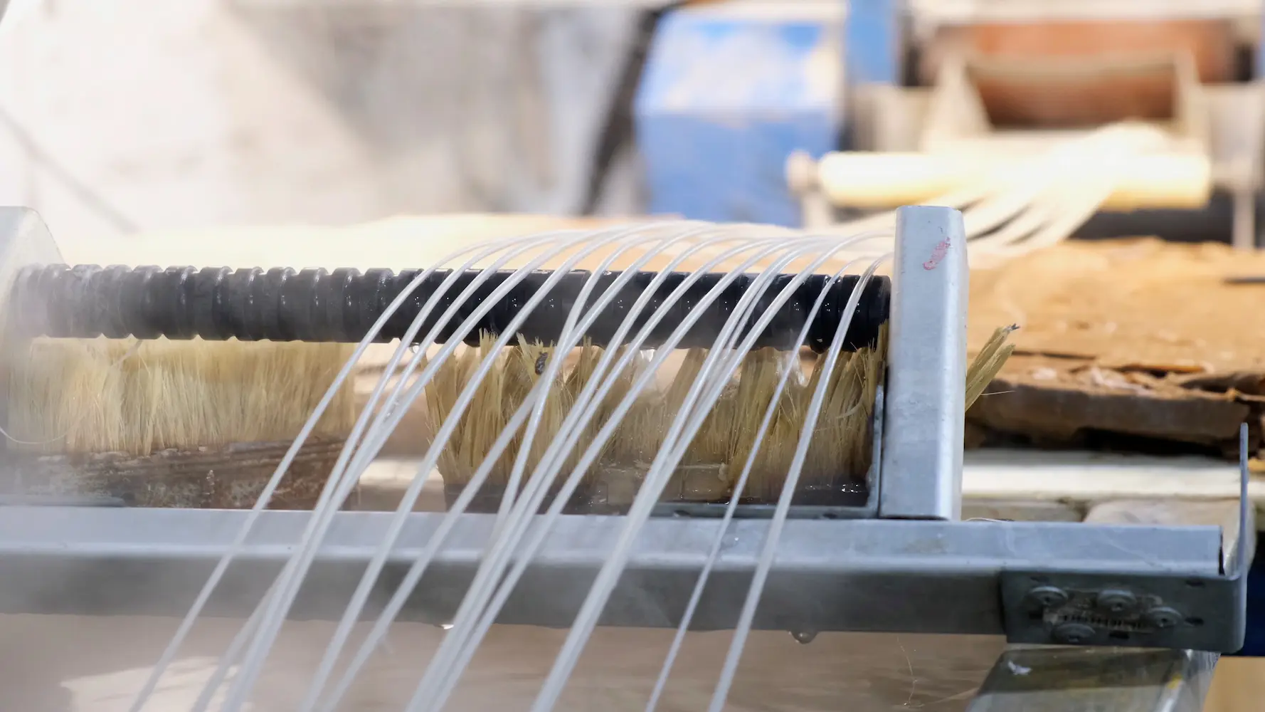 Close-up of a water filtration system with multiple transparent tubes aligned over a brush mechanism. The setup appears to be part of an industrial water purification process.