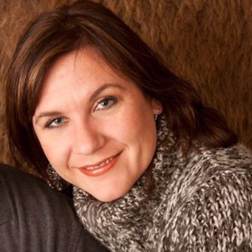 A woman with brown hair, wearing a grey patterned sweater, smiles at the camera. The background is brown and textured.