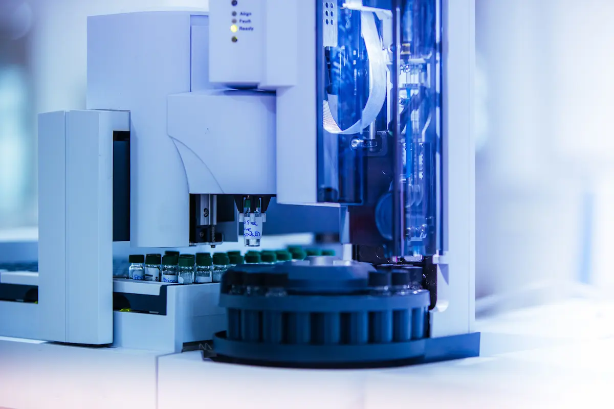 A close-up of a modern laboratory machine with vials and a robotic arm used for automated chemical analysis or testing.