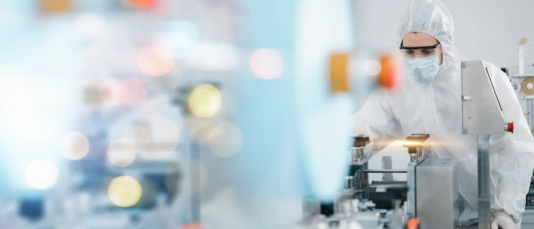 A person wearing protective gear operates machinery in a cleanroom or laboratory environment.