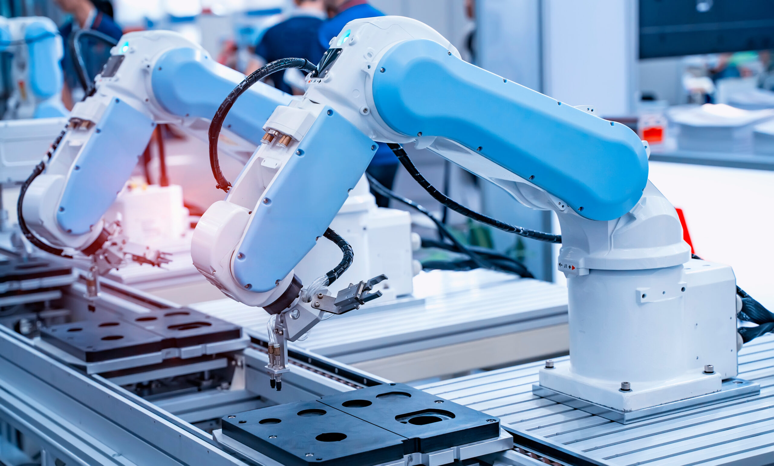 Two robotic arms on an assembly line in a manufacturing setting.